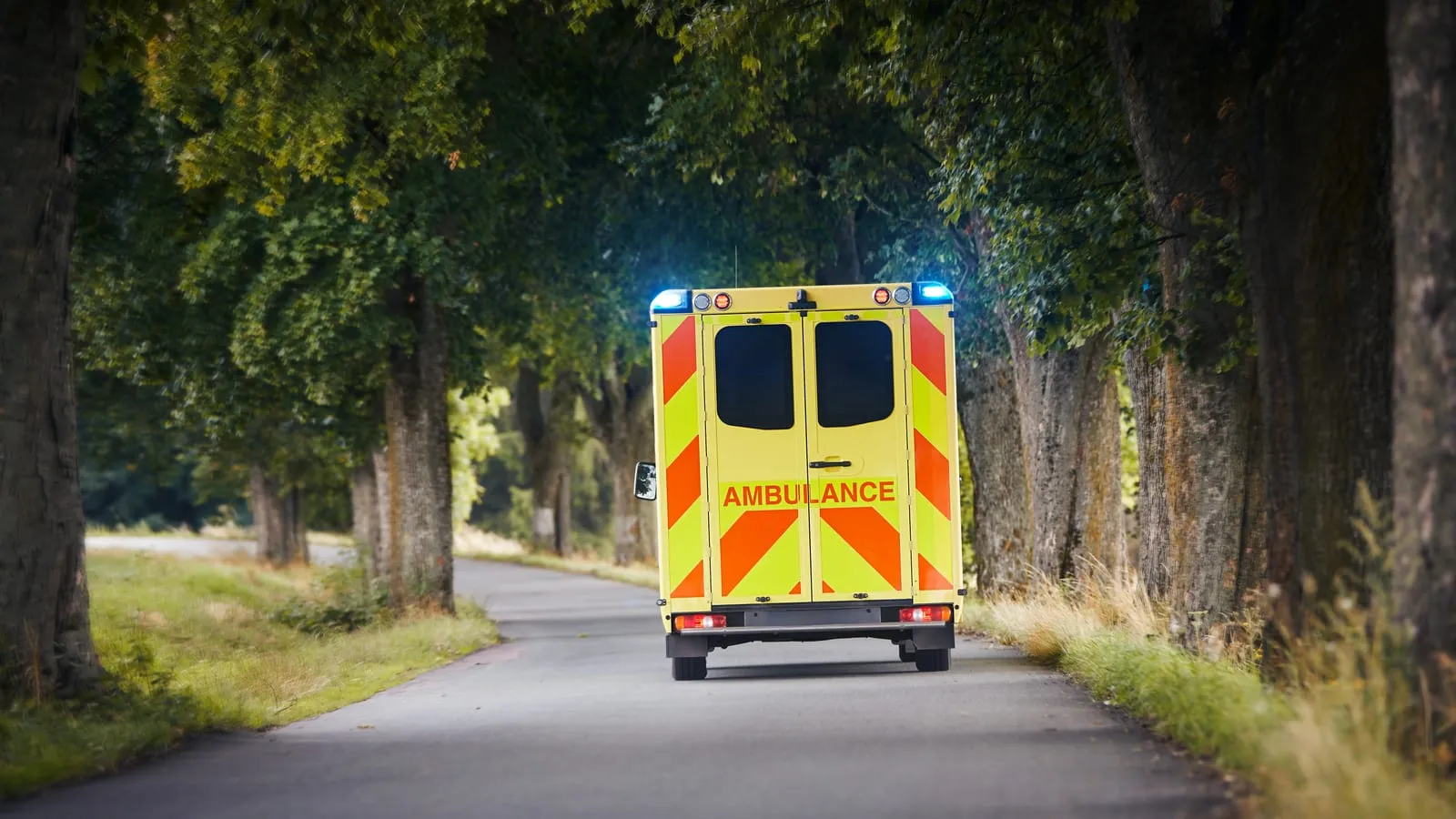 Ambulance driving on a tree-lined road for C1 training across the North West